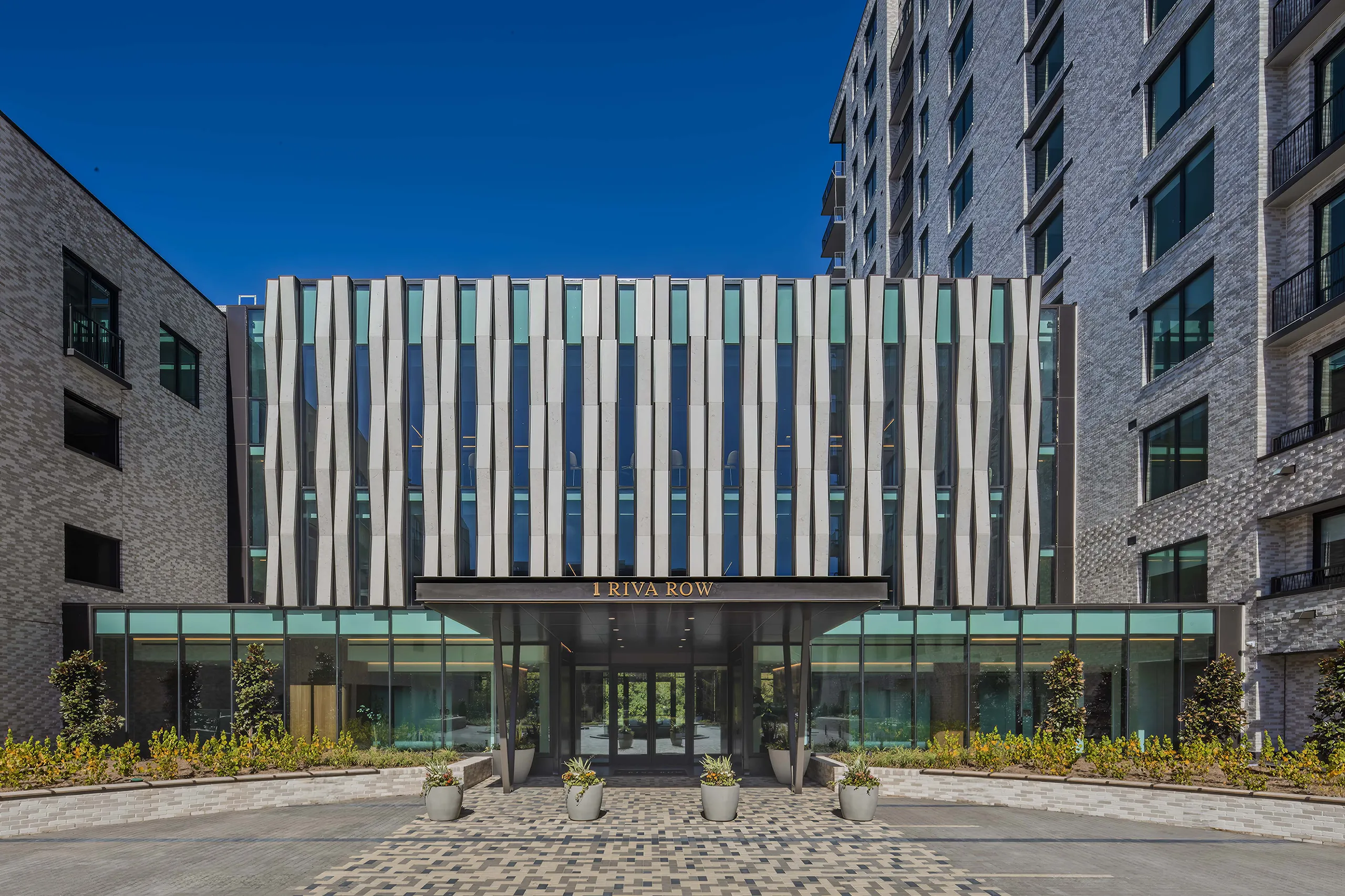 Riva Row apartment complex with modern high-rise architecture, featuring large windows and balconies along the canal walkway at sunset.